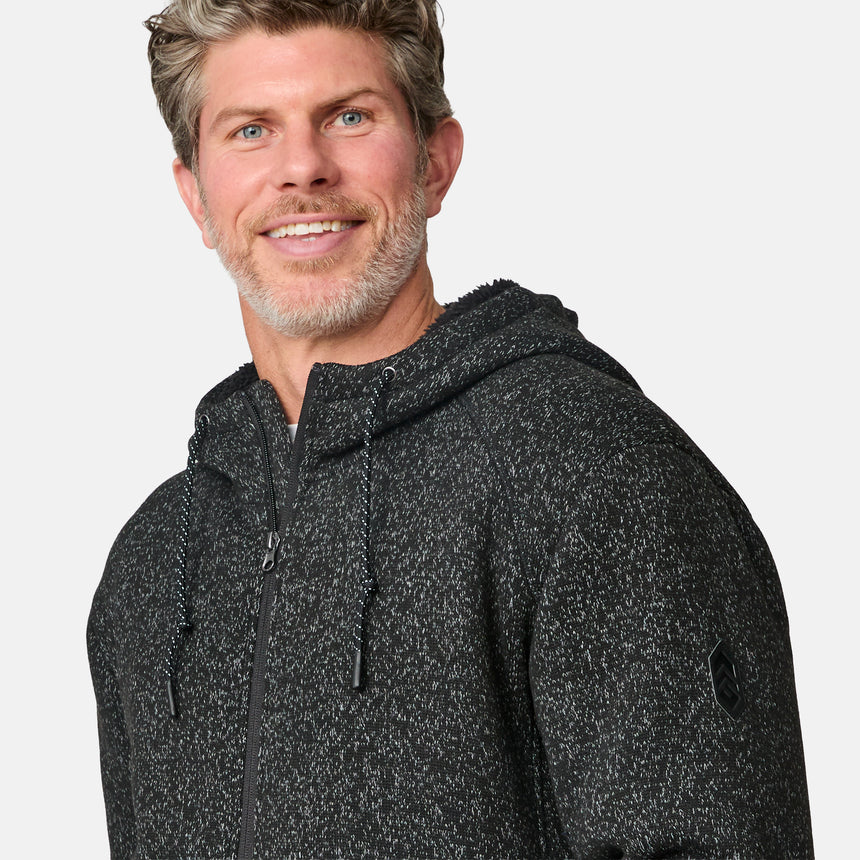 [Kolby is 6’2” wearing a size Medium.] Man wearing the Free Country Men's Northwood Mountain Fleece Hoodie in heather black with black drawstrings, standing with hands in pockets against a plain, light background.
