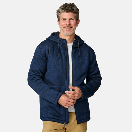 [Kolby is 6’2” wearing a size Medium.] Man wearing the Free Country Men's Northwood Mountain Fleece Hoodie in heather navy with black drawstrings, standing with hands in pockets against a plain, light background.