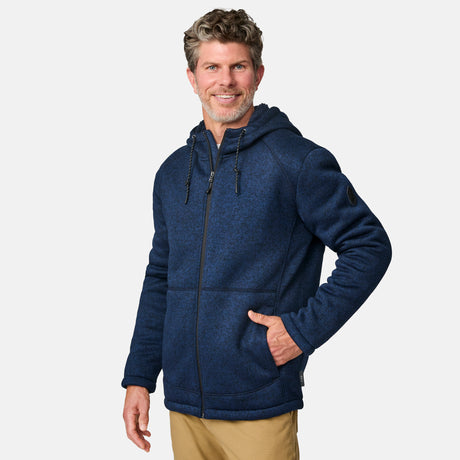 [Kolby is 6’2” wearing a size Medium.] Man wearing the Free Country Men's Northwood Mountain Fleece Hoodie in heather navy with black drawstrings, standing with hands in pockets against a plain, light background.