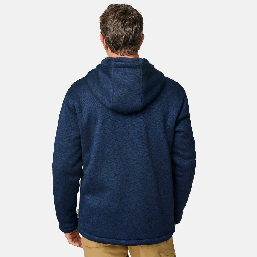 [Kolby is 6’2” wearing a size Medium.] Man wearing the Free Country Men's Northwood Mountain Fleece Hoodie in heather navy with black drawstrings, standing with hands in pockets against a plain, light background.