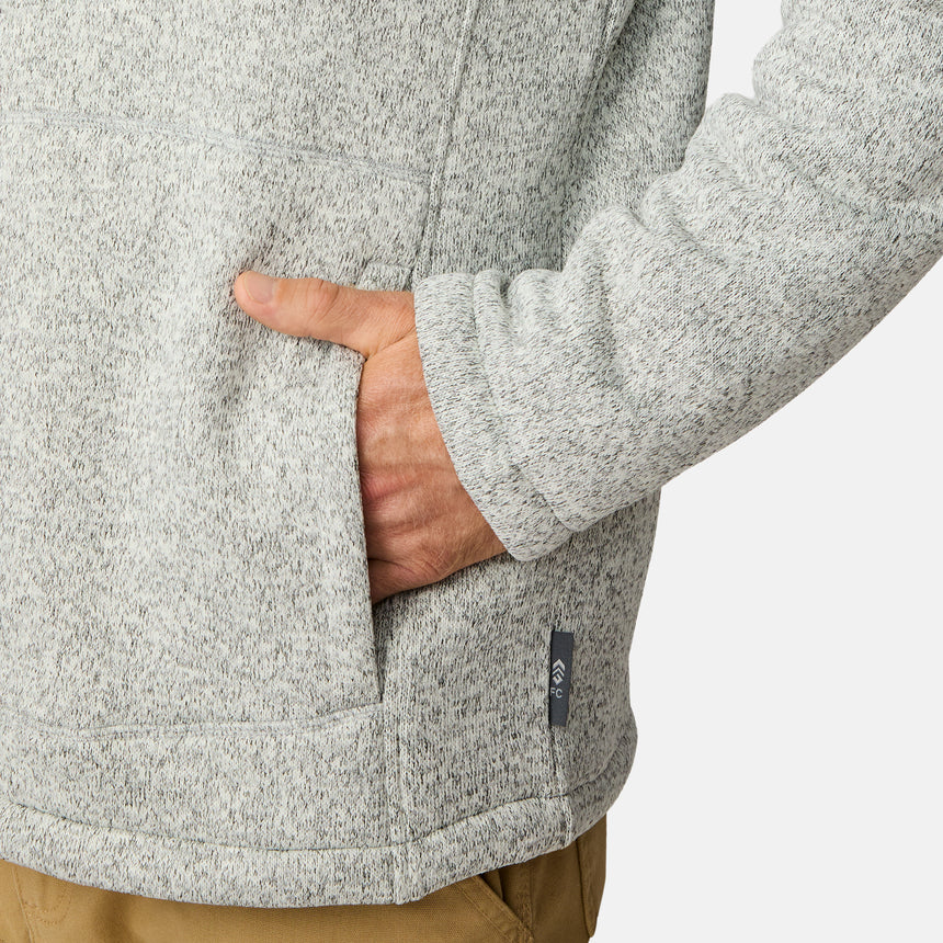 [Kolby is 6’2” wearing a size Medium.] Man wearing the Free Country Men's Northwood Mountain Fleece Hoodie in light gray with black drawstrings, standing with hands in pockets against a plain, light background.