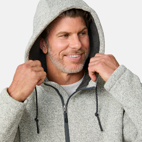 [Kolby is 6’2” wearing a size Medium.] Man wearing the Free Country Men's Northwood Mountain Fleece Hoodie in light gray with black drawstrings, standing with hands in pockets against a plain, light background.