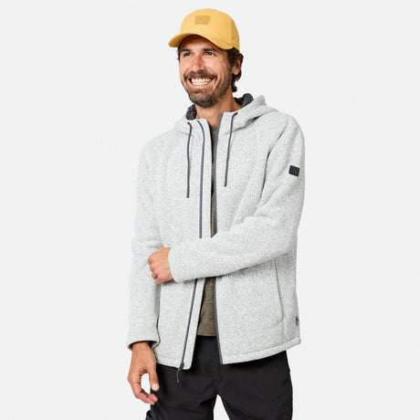 [Model is wearing size M.] A smiling man in a yellow cap, dark pants, and a light gray Men’s Mountain Fleece Jacket from Free Country stands against a plain white background, his left hand relaxed while his right hand holds the jacket zipper.