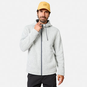 [Model is wearing size M.] A man wearing a pumice-colored Free Country Men’s Mountain Fleece Jacket and a yellow cap stands against a plain white background, adjusting the jacket collar with one hand while the other rests at his side.