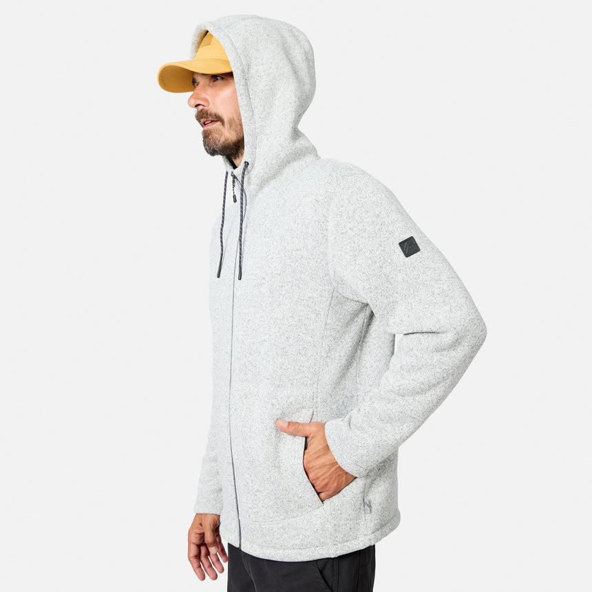 [Model is wearing size M.] A man wearing a light gray Free Country Men’s Mountain Fleece Jacket with the hood up, a yellow cap, and dark pants stands facing left with his hands in his pockets against a plain white background.