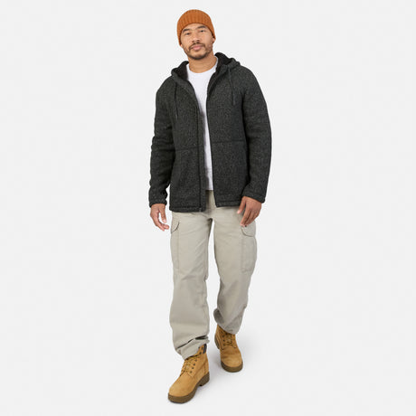 A man in an orange beanie, a dark grey Free Country Men’s Mountain Fleece over a white t-shirt, light-colored cargo pants, and tan boots walking forward.