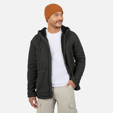 A man wearing a charcoal textured Free Country Men’s Mountain Fleece Jacket zip-up hoodie over a white t-shirt, tan cargo pants, and a burnt-orange knit beanie.