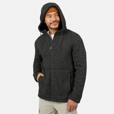 A man wearing a black heather Free Country Men’s Mountain Fleece jacket with a drawstring hood and front pockets, layered over a white t-shirt and an orange beanie.