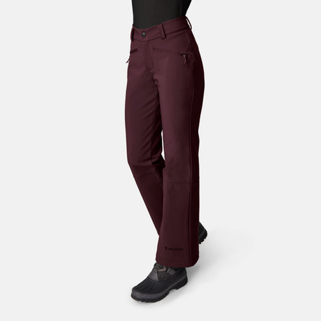 A person wears Free Country Women’s Stormlite Super Softshell® Ski Pants in dark burgundy, featuring water resistance, zippered pockets, and a slight flare at the hem, paired with black boots. Only the lower half is visible against a light background.