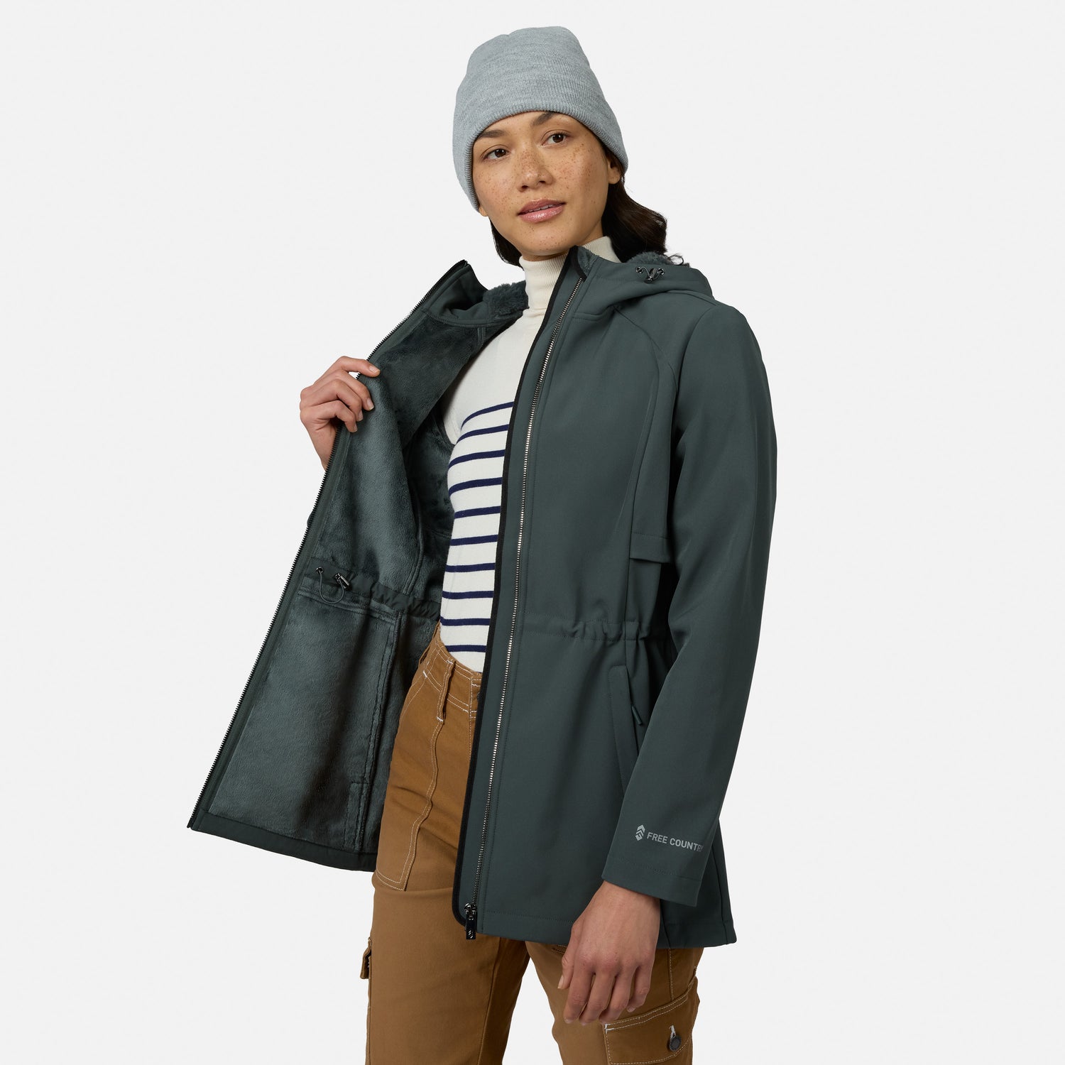 [Model is wearing size S.] A woman wearing a dark gray hooded waterproof jacket, a gray beanie, a white and navy striped turtleneck, and brown pants, shown against a light gray studio background.