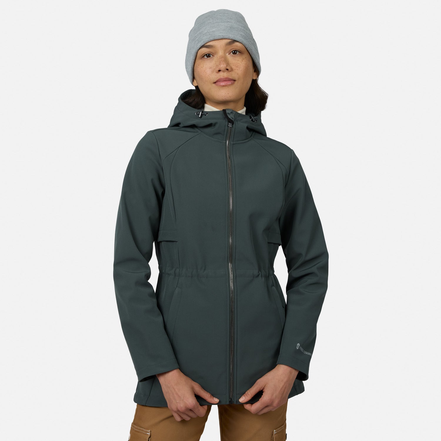 [Model is wearing size S.] A woman wearing a dark slate green hooded jacket, a light gray beanie, and tan pants, standing against a light gray studio background.