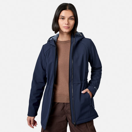 A woman modeling a navy blue hooded jacket over a brown sweater and brown pants, photographed against a clean light gray studio background.