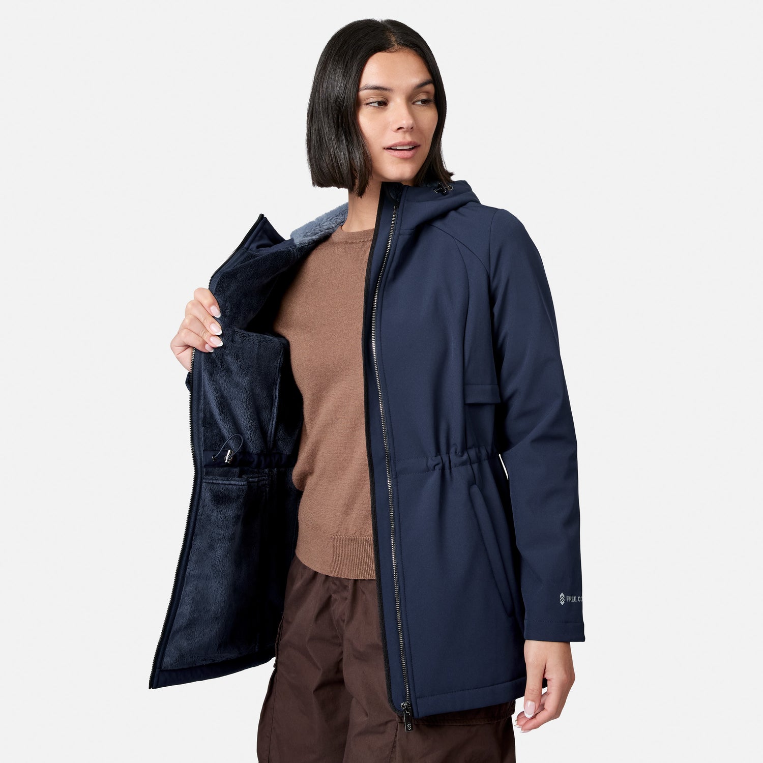 [Model is wearing size S.] A woman modeling a navy hooded jacket with a dark brown knit top and brown pants, holding open the jacket to show the dark navy fleece-lined interior against a light gray background.