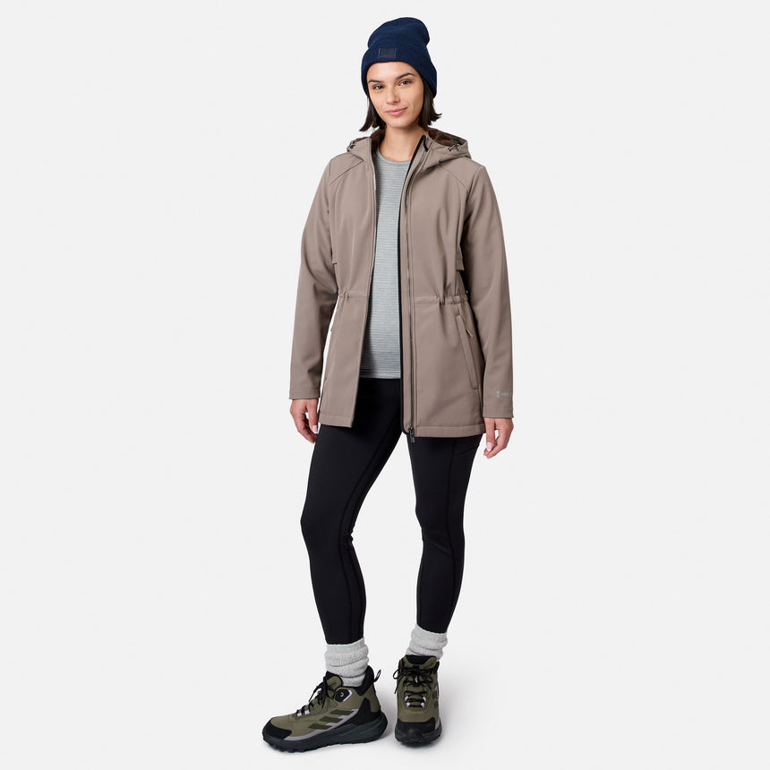 [Model is wearing size S.] A woman modeling a light brown hooded jacket, black leggings, a gray shirt, a navy beanie, and hiking boots against a light gray background.