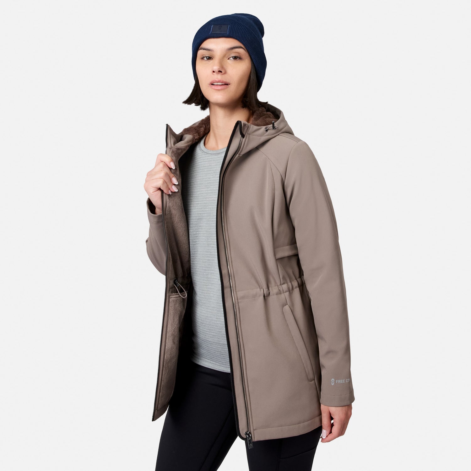 [Model is wearing size S.] A woman modeling a hooded insulated jacket in taupe-brown, worn over a light gray ribbed top and black pants, with a navy beanie. The jacket has a brown faux-fur lined hood and a drawcord waist, shown against a light gray studio background.
