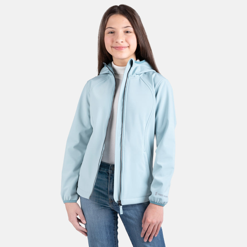 [Samantha is wearing size M.] Model wearing a Free Country light blue softshell zip-front hooded jacket with a smooth, weather-resistant finish, side pockets, and tonal stitching—layered over a white turtleneck and paired with blue jeans for a clean, casual winter look.