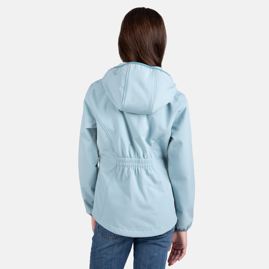 [Samantha is wearing size M.] Model wearing a Free Country light blue softshell zip-front hooded jacket with a smooth, weather-resistant finish, side pockets, and tonal stitching—layered over a white turtleneck and paired with blue jeans for a clean, casual winter look.