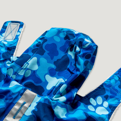 A close-up of the Free Country Dog Raincoat, featuring blue camouflage and paw prints, waterproof fabric, a hood, and Velcro straps, set against a plain light grey background.