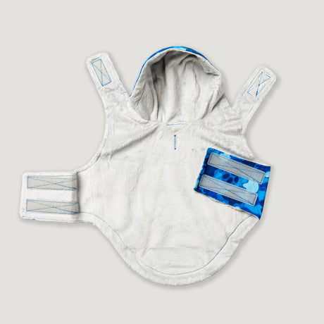 The Free Country Dog Raincoat is a soft, white, hooded waterproof jacket with three Velcro straps and a blue patterned pocket, shown laid flat on a light background.