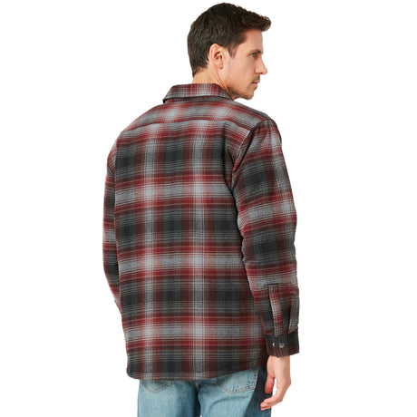 A man wearing the Clearance Men's FreeCycle® Utility Work Shirt in a black, gray, and red plaid made with eco-conscious REPREVE fabric and blue jeans stands with his back to the camera, glancing over his shoulder.