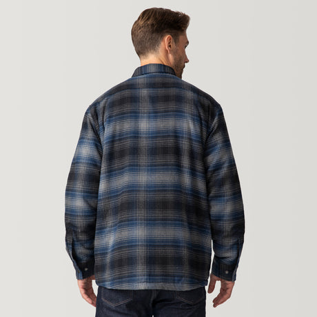 A man faces away from the camera, wearing a Clearance Men's Flannel Workwear Shirt with a blue and black plaid print and dark jeans, set against a plain light gray background.