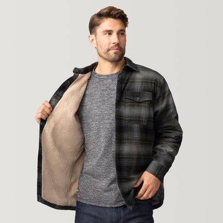 A man wears the Clearance Men's Flannel Workwear Shirt, a black and green plaid jacket with a beige sherpa lining, over a gray T-shirt and blue jeans. He stands against a plain light background, showing the jacket's interior.
