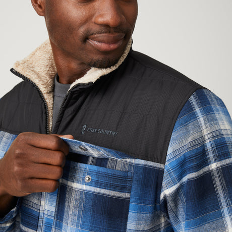 [Model is wearing a size Medium.] Man wearing Free Country Men's Woodsman Work Jacket in blue and white plaid with a full front zipper opening, soft lining, and recycled polyester filling, light grey background. Perfect men’s jacket for fall weather.
