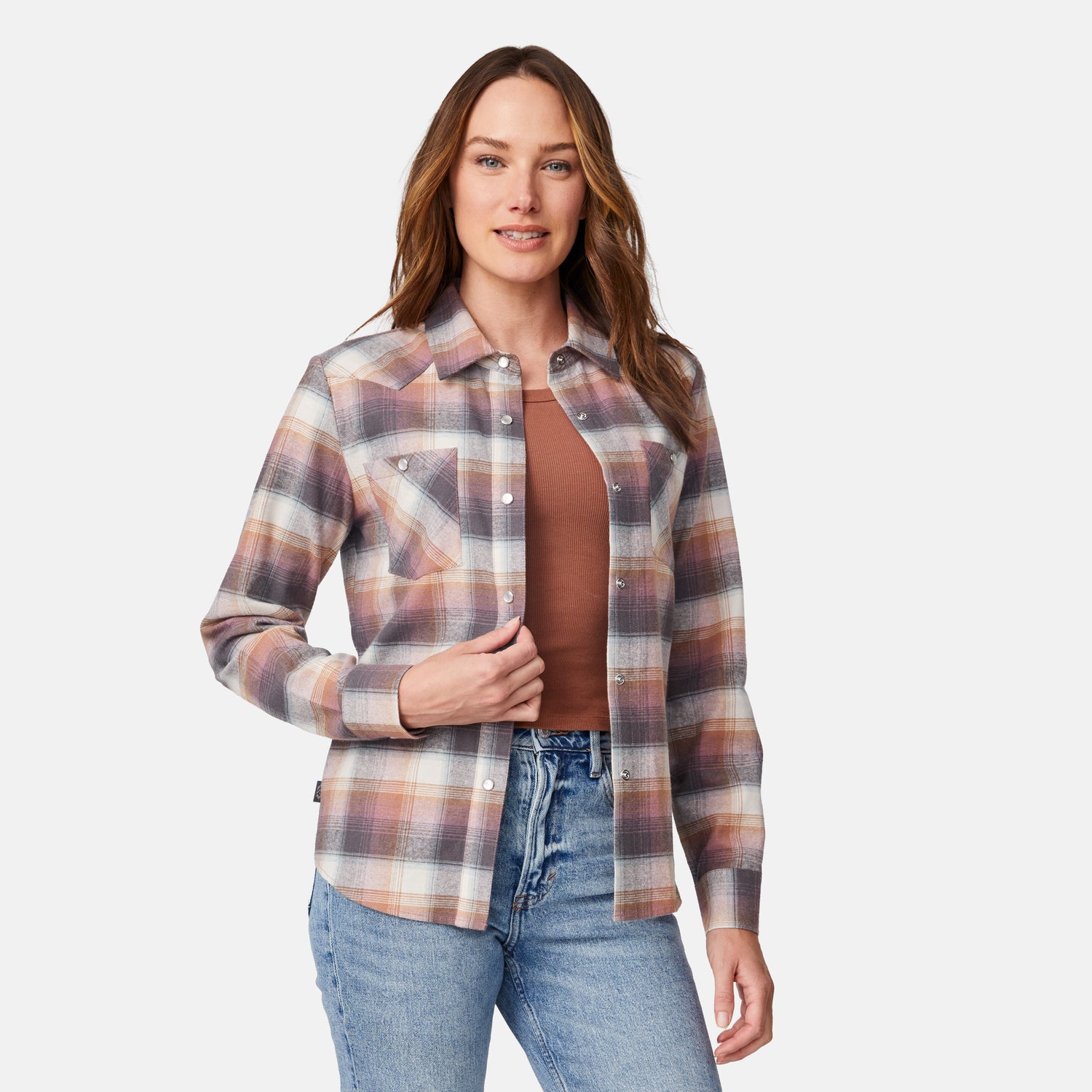 [Model is wearing size S.] A woman modeling a long-sleeve button-up plaid shirt in muted brown, beige, and gray tones, worn over a rust-brown top and blue jeans against a light gray studio background.