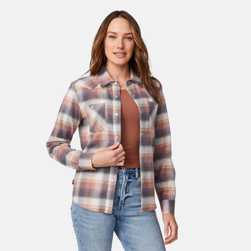 [Model is wearing size S.] A woman modeling a long-sleeve button-up plaid shirt in muted brown, beige, and gray tones, worn over a rust-brown top and blue jeans against a light gray studio background.