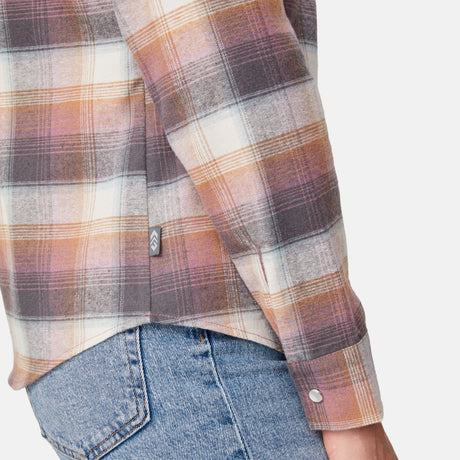 [Model is wearing size S.] Close-up of a person wearing a long-sleeve plaid flannel shirt in muted orange, brown, cream, and gray tones, paired with blue jeans against a light gray background.