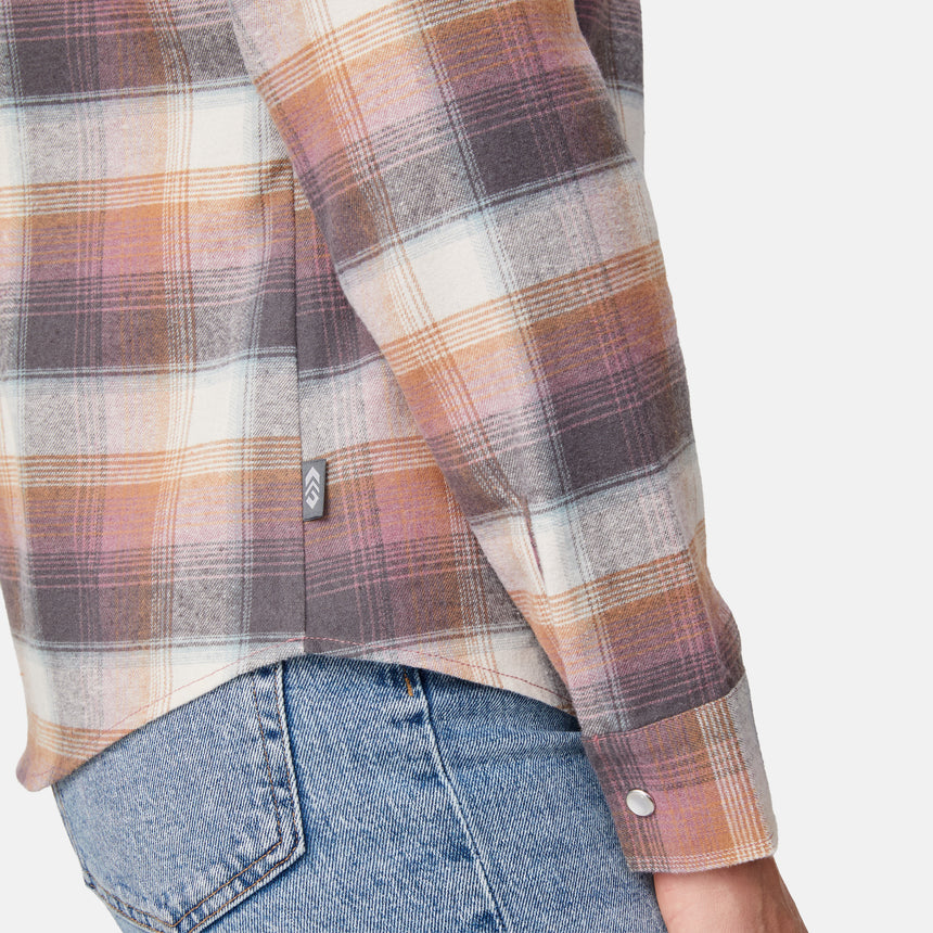 [Model is wearing size S.] Close-up of a person wearing a long-sleeve plaid flannel shirt in muted orange, brown, cream, and gray tones, paired with blue jeans against a light gray background.