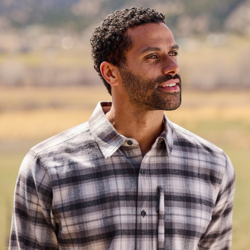 Man wearing a plaid shirt outdoors with a blurred natural background
