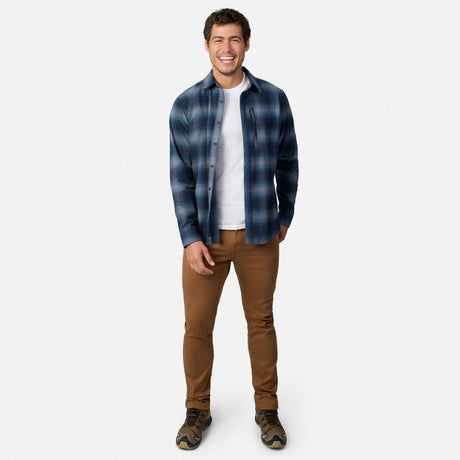 [Model is wearing size M.] A man modeling a blue and gray plaid button-down shirt over a white t-shirt, paired with brown pants and hiking boots, against a light gray background.
