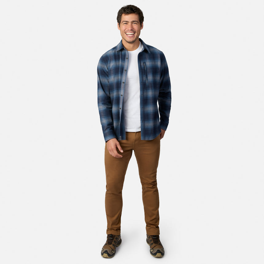 [Model is wearing size M.] A man modeling a blue and gray plaid button-down shirt over a white t-shirt, paired with brown pants and hiking boots, against a light gray background.