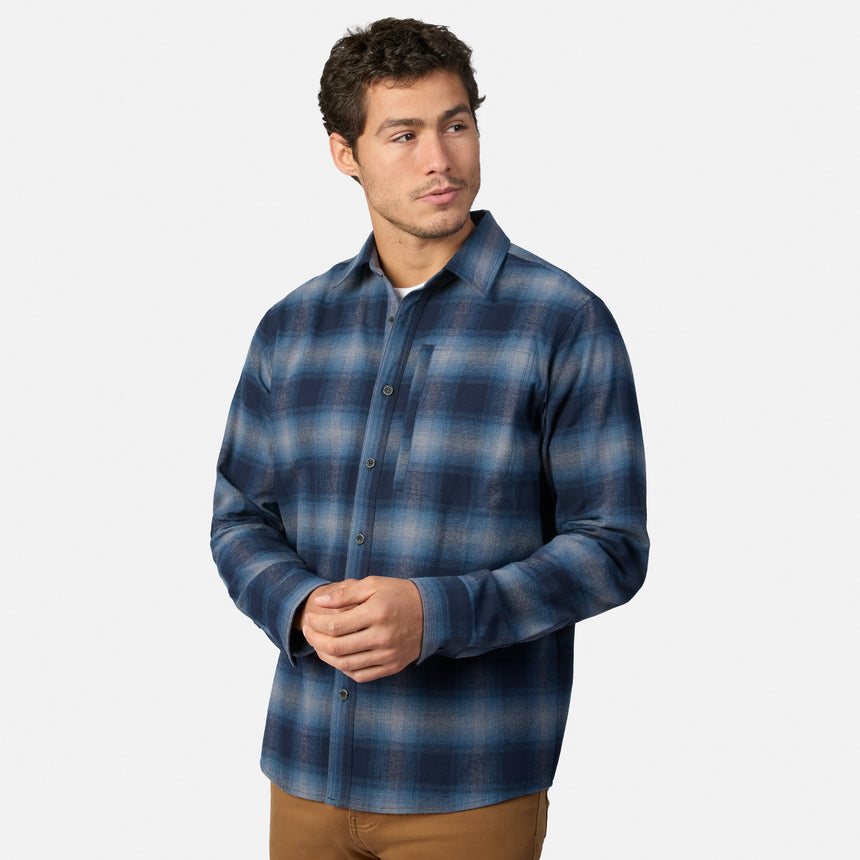 [Model is wearing size M.] A man wearing a blue and navy plaid long-sleeve button-up shirt, paired with brown pants, standing against a light gray background.