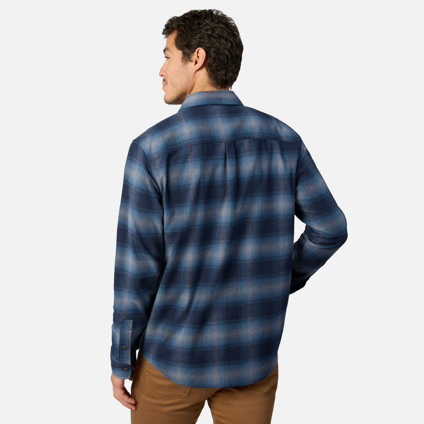 [Model is wearing size M.] A man wearing a blue and gray plaid long-sleeve button-down shirt, shown from a rear three-quarter view against a light gray background.