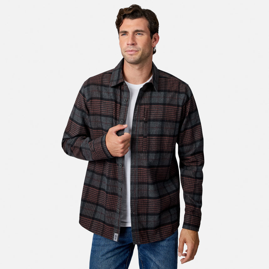 [Model is wearing size M.] A man wearing a dark gray and brown plaid button-down flannel shirt over a white t-shirt and blue jeans, standing against a light gray studio background.