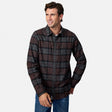 [Model is wearing size M.] A man wearing a dark brown and black plaid button-down flannel shirt with blue jeans, standing against a light gray background.