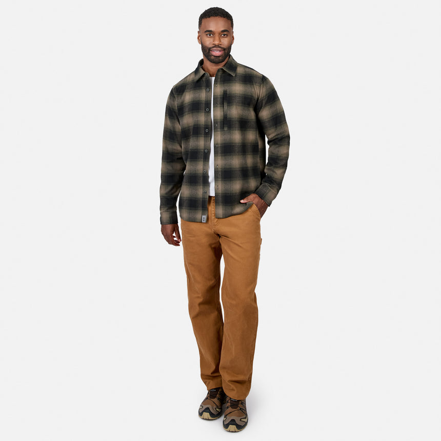 [Model is wearing size M.] A man modeling a dark green and black plaid button-down flannel shirt with brown pants, standing against a light gray studio background.