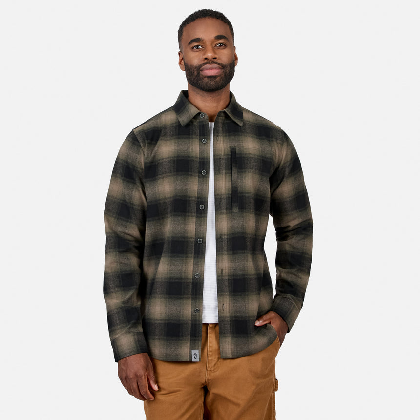 [Model is wearing size M.] A man wearing a long-sleeve plaid button-up shirt in dark green and brown tones, layered over a white t-shirt and paired with tan pants, against a light gray background.