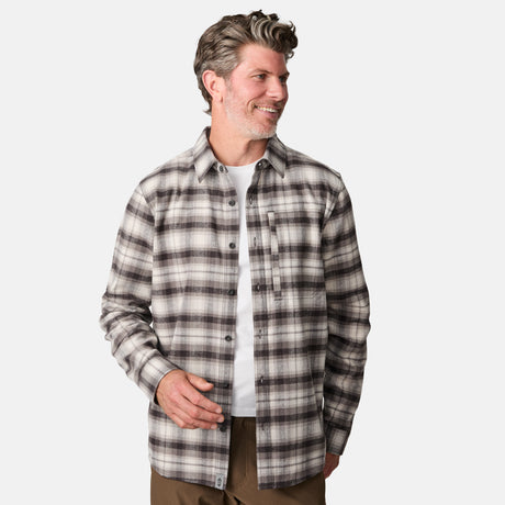 A man with wavy brown and gray hair wears a white T-shirt under the Free Country Men's Easywear Flannel Shirt in gray and brown, featuring a chest zipper pocket, paired with brown pants, smiling against a plain white background.