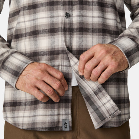 A person buttons a brown and gray plaid Men's Easywear Flannel Shirt by Free Country, paired with brown pants. Only the torso and hands are visible in the image.