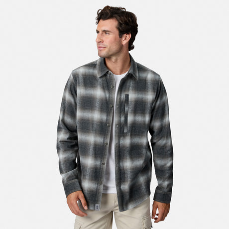 [Model is wearing size M.] A man wearing a dark gray and black plaid button-down shirt over a white t-shirt and beige pants, photographed against a light gray studio background.