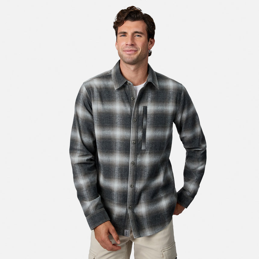 [Model is wearing size M.] A man wearing a long-sleeve button-up flannel shirt with a gray and black plaid pattern, paired with light beige pants, against a plain light gray background.
