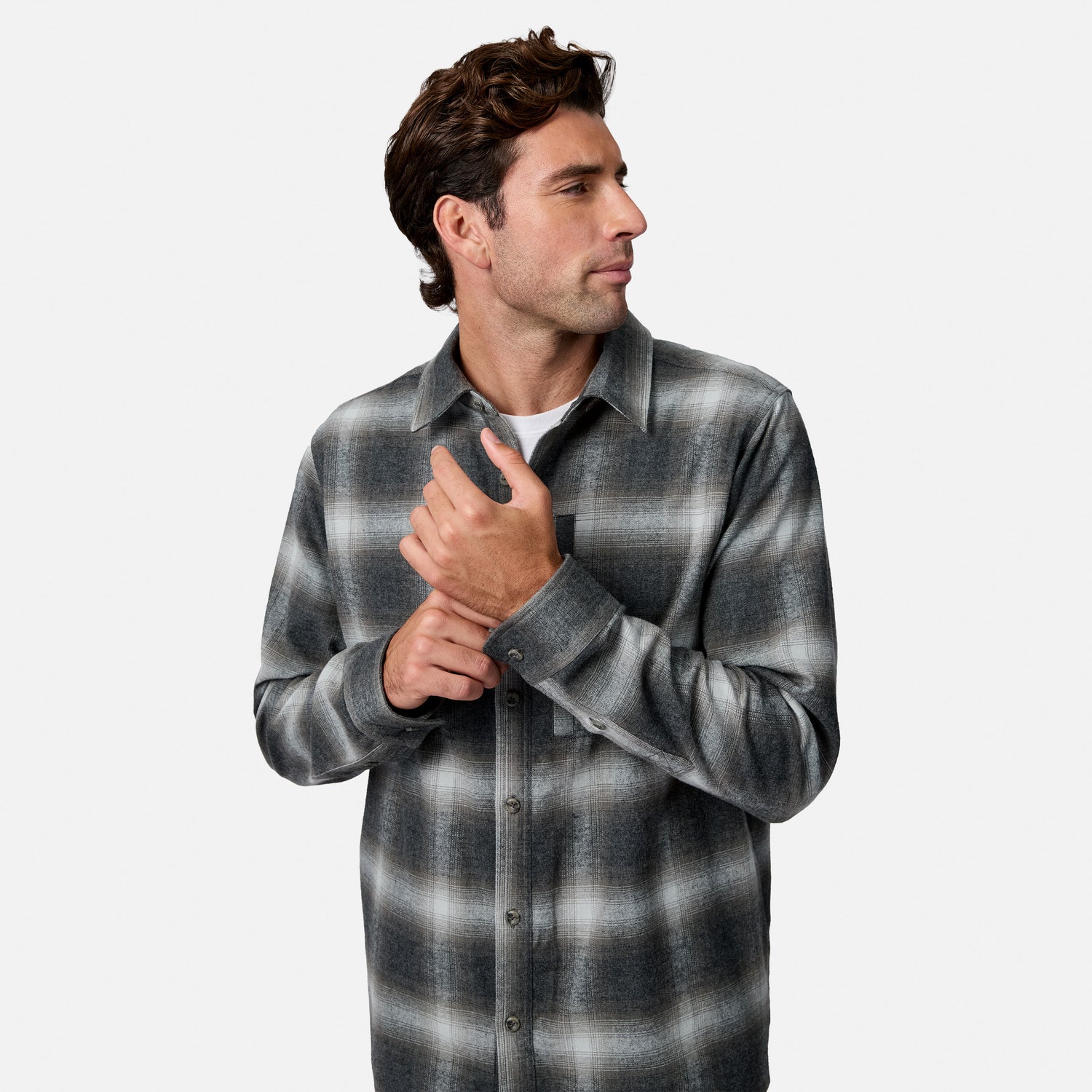 [Model is wearing size M.] A man wearing a gray and black plaid button-down shirt over a white undershirt, shown from the waist up against a light gray studio background.