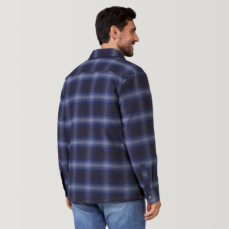 A man with dark hair, seen from behind, wears the Clearance Men's FreeCycle® Utility Work Shirt in blue and navy plaid with blue jeans, standing against a plain light-colored background.