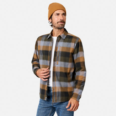 [Model is wearing size M.] A man wearing a brown, gray, and black plaid button-up flannel shirt over a white t-shirt, paired with blue jeans and a tan beanie, photographed against a light gray studio background.