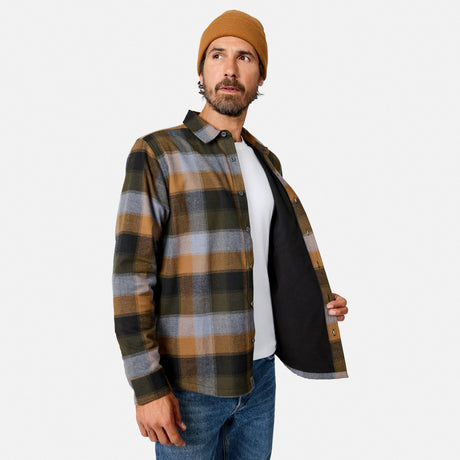 [Model is wearing size M.] A man wearing a brown, black, and gray plaid flannel shirt over a white t-shirt and blue jeans, with a tan beanie, holding the shirt open to show the black lining against a light gray background.