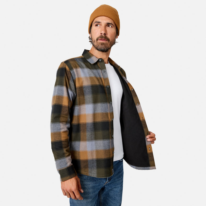 [Model is wearing size M.] A man wearing a brown, black, and gray plaid flannel shirt over a white t-shirt and blue jeans, with a tan beanie, holding the shirt open to show the black lining against a light gray background.
