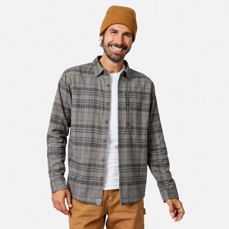 [Model is wearing size M.] A smiling man wearing a gray and black plaid button-up flannel shirt over a white t-shirt, paired with a tan beanie and tan pants, against a light gray background.